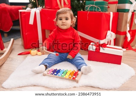 Adorable hispanic toddler playing xylophone sitting on floor by christmas gifts at home