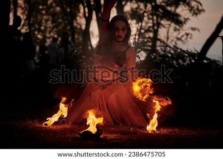 Girl fire dancing performance at outdoor art festival, smooth movements of female fire show artist with bowl. Woman dancing with fire flame art performance, twilight forest background Royalty-Free Stock Photo #2386475705
