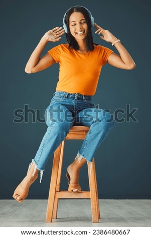 Woman, headphones and listening to music while dancing and streaming online on a studio background. Happy gen z person with headset for podcast, radio or audio sound on chair to relax for freedom