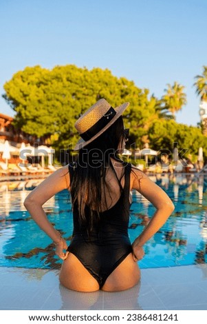 Elegant Woman in Swimsuit Relaxing by Resort Pool with Sun Hat Looking at Sunset