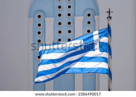 View of the greek flag waving in the air and a whitewashed church in the background in Ios Greece