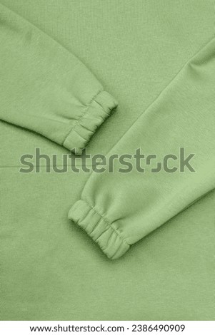 Green background of warm knitted sweatshirt and sleeves with elastic bands, concept of comfort and sport.