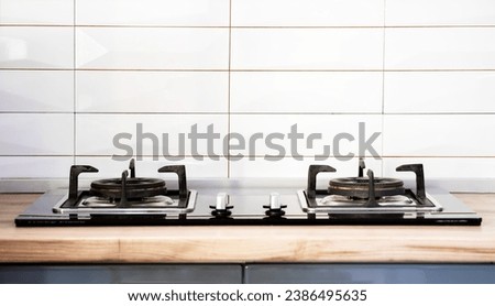 Front view of Contemporary tempered glass gas stove hob with Two burners with auto ignition knob on wooden countertop, cast iron pan supports fan hood and oven built in compact Royalty-Free Stock Photo #2386495635