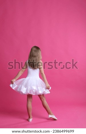 Cute little girl in white dress dancing on pink background, back view