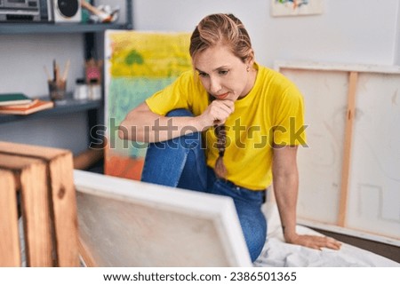 Young blonde woman artist looking draw with serious expression at art studio