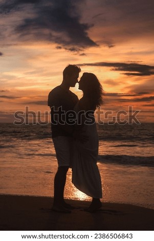 Silhouettes of couple in love togetherness posing at tropical sea sunset, full body. Male and female kissing and embracing on sandy beach outside. Summer vacation lifestyle concept. Copy ad text space