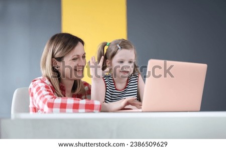 Mother and little daughter are sitting in front of laptop and waving. Remote communication during covid 19 pandemic concept Royalty-Free Stock Photo #2386509629