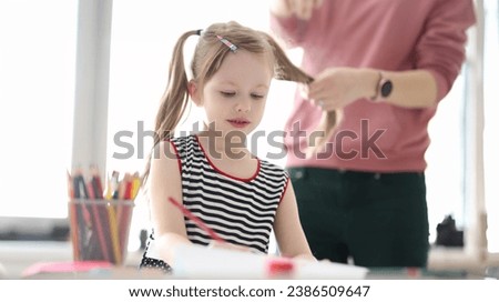 Little girl drawing with pencils. Mother braiding child hair. Childcare concept