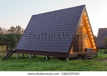 The concept of glamping and renting a chalet for weekend. Wooden house with a veranda in nature around coniferous trees. Royalty-Free Stock Photo #2386539343