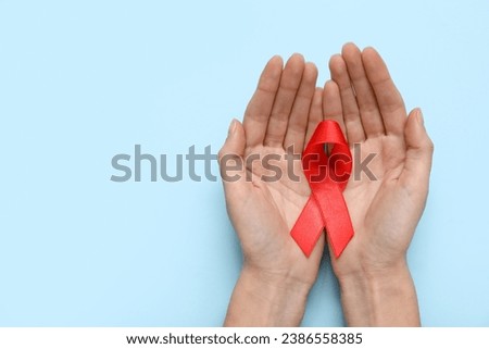 Woman with red ribbon on blue background. AIDS Day concept Royalty-Free Stock Photo #2386558385