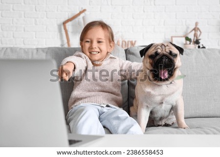 Little girl with cute pug dog watching cartoons at home