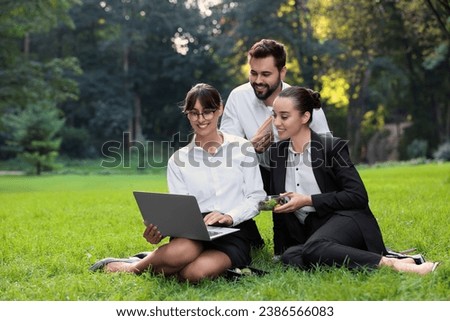 Happy colleagues with laptop having business lunch on green grass in park