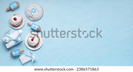Tasty donuts, dreidels, Jewish hat and gifs on light blue background with space for text. Hannukah celebration Royalty-Free Stock Photo #2386571863