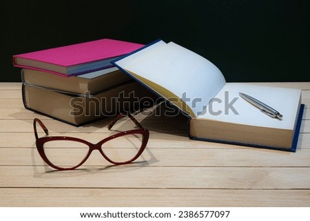 Stack of books with eye-glasses and pen on a table. Still-life photo, made on studio with black background and softbox