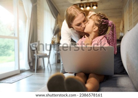 Mother kissing her little daughter who taking lessons online