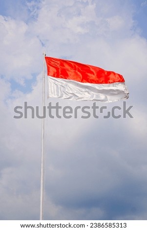 a red and white flag flying on a pole against a background of a sky full of clouds. 
