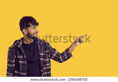 Happy positive smiling young indian man looking and pointing aside with finger hand gesture at copy space advertising product, sale discount promo offer standing isolated on yellow background.