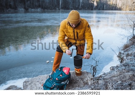 Guy tourist cooking food on a hike on a gas burner, mobile system for cooking in the field, trekking in nature in the mountains. High quality photo