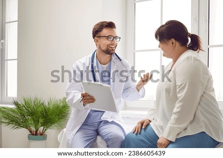 Portrait of fat overweight female patient in medical office listening to a friendly doctor holding report file with appointment and giving consultation a woman during medical examination in clinic. Royalty-Free Stock Photo #2386605439