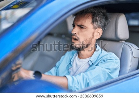 Young hispanic man stressed driving car at street Royalty-Free Stock Photo #2386609859