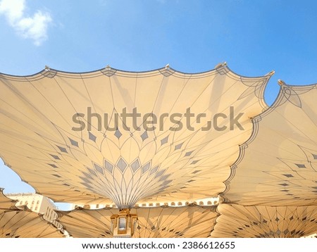 minaret or minaret and large umbrella umbrellas blooming at the nabawi mosque saudi arabia in a sunny day with a blue sky. as background, poster, wallpaper.
