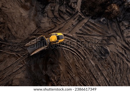 Aerial view directly above an industrial dumper truck or earth mover vehicle with muddy soil and tyre tracks in the construction industry on a brownfield site with copy space