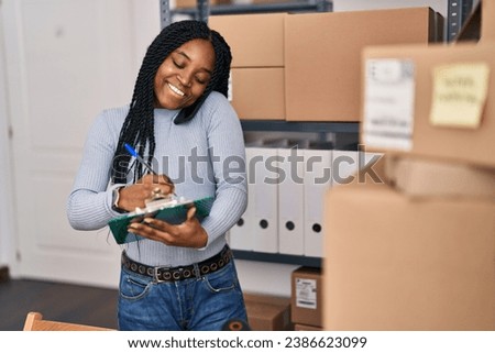 African american woman ecommerce business worker writing on document talking on smartphone at office