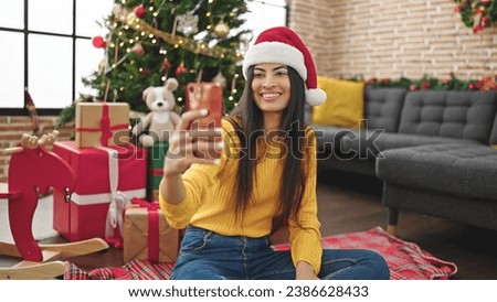 Young beautiful hispanic woman celebrating christmas taking selfie picture by smartphone at home
