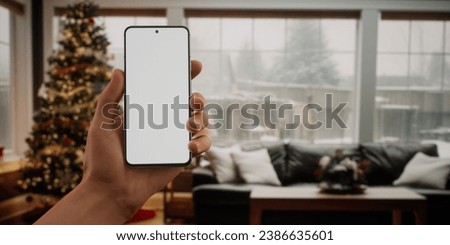 CU Caucasian man checking his phone near Christmas tree. Blank screen phone mockup. Holiday shopping
