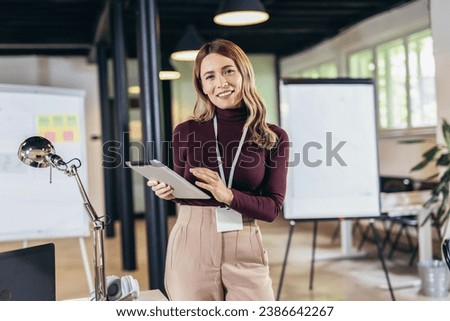 Smiling businesswoman standing in modern office with digital tablet.