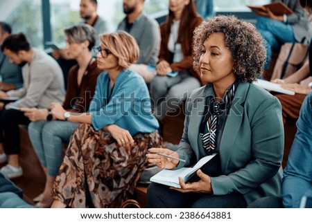 Mature businesswoman taking notes while participating in an education event at convention center. Royalty-Free Stock Photo #2386643881