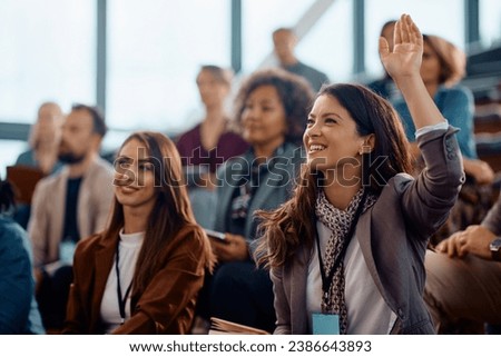 Happy businesswoman raising hand to ask a question attending a seminar in conference hall. Royalty-Free Stock Photo #2386643893
