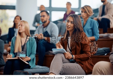 Female entrepreneur taking notes while attending a business seminar in conference hall.