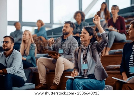 Happy businesswoman raising her arm to answer the question during education event in conference hall.  Royalty-Free Stock Photo #2386643915