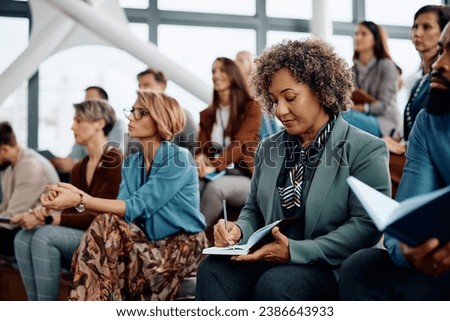 Mature entrepreneur writing in her notebook while attending a business seminar at conference hall. Royalty-Free Stock Photo #2386643933