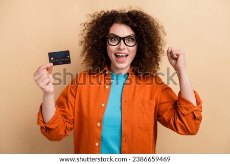 Photo portrait of attractive young woman credit card raise fist celebrate dressed stylish orange clothes isolated on beige color background