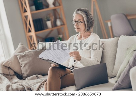 Photo of pretty attentive senior lady accountant dressed white cardigan reading documents clipboard indoors house room