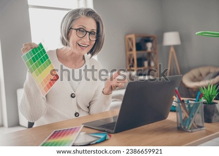 Photo of shiny positive elderly lady designer wear white cardigan showing customer new interior colors indoors apartment room