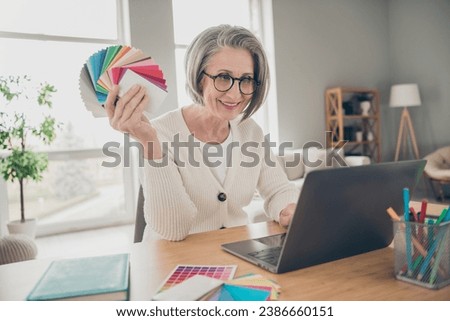 Photo of shiny adorable elderly lady wear white choosing colors palette modern device indoors apartment room