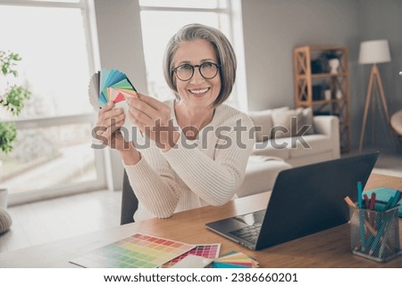 Photo of cheerful positive senior lady dressed white cardigan picking new walls colors holding palette indoors house room