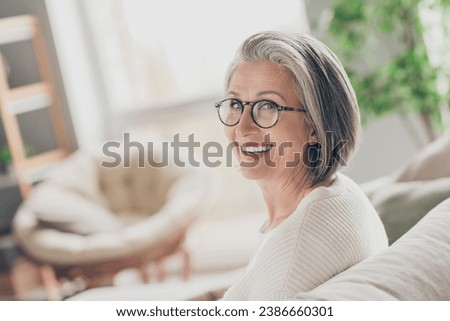 Photo of charming good mood elderly lady wear white cardigan spectacles smiling indoors apartment room Royalty-Free Stock Photo #2386660301