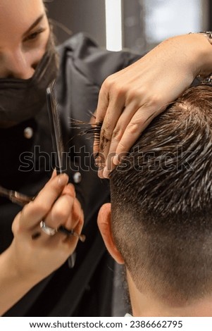 Close-up, side view, hairdresser using scissors and comb doing a man's haircut. Step-by-step haircut training. Barber at work. There is no face. Modern hairdressing salon, barbershop concept