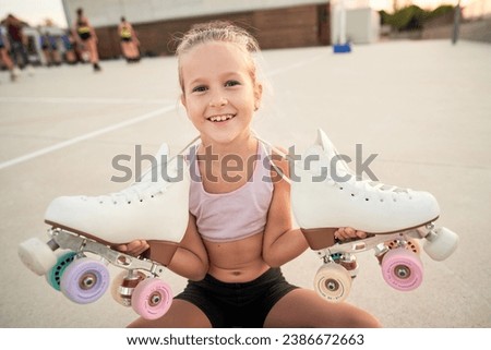 Smiling child in activewear holding quad roller skates and looking at camera after training in skate park