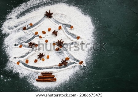 Christmas tree with star of anise, sultans or yellow raisins, and cinnamon bark on a white flour over green background. Table top view