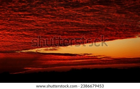 Beautiful colorful dramatic sky with cloud at sunset or sunrise. Bright colorful sunset over silhouettes of residential buildings in cottage village. Beautiful landscape in bright colors of sunset sky