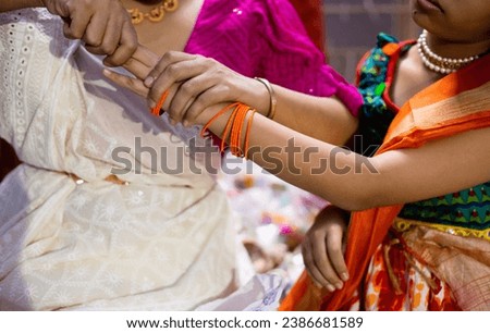 An Indian mother helping her girl child to wear traditional ornaments bangles indoors at a festival night Royalty-Free Stock Photo #2386681589