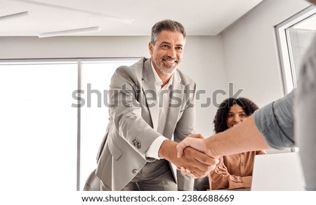 Happy older middle aged senior businessman leader shaking hand of new male partner, client or customer making sales deal at team executive board meeting in conference room. Business handshake concept. Royalty-Free Stock Photo #2386688669