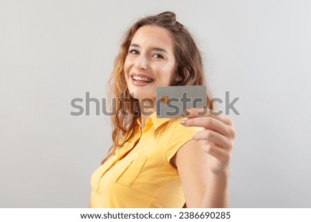 Portrait of laughing girlish woman with long hair do wear yellow top. Hand showing credit card isolated on white background