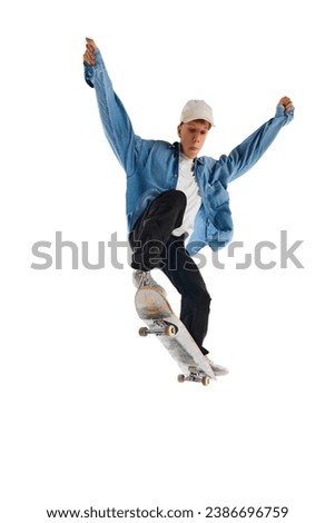 Teen boy in blue jeans shirt and cap in motion, training with skateboard, doing stunts isolated over white background. Concept of professional sport, competition, training, action. Copy space for ad