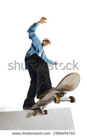 Bottom view image of teen boy in casual clothes in motion, training, doing stunts on skateboard isolated over white background. Concept of professional sport, competition, training, action. Royalty-Free Stock Photo #2386696763